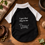 White and black raglan dog shirt laid flat, printed I got that dog in me above a dachshund drawn as a chimney cake