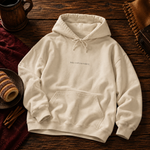 Sand hoodie with Bake it till you make it printed small on the chest, on a wooden table beside chimney cakes